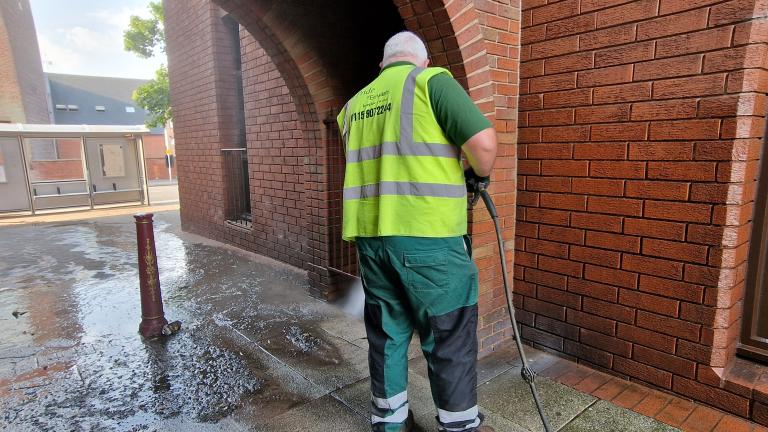 A council employee in a high vis vest power washes paving