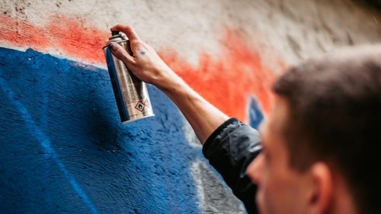 A person with a can of spray-paint graffities a wall