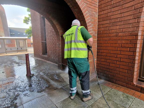 A council employee in a high vis vest power washes paving