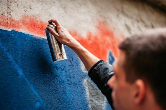 A person with a can of spray-paint graffities a wall